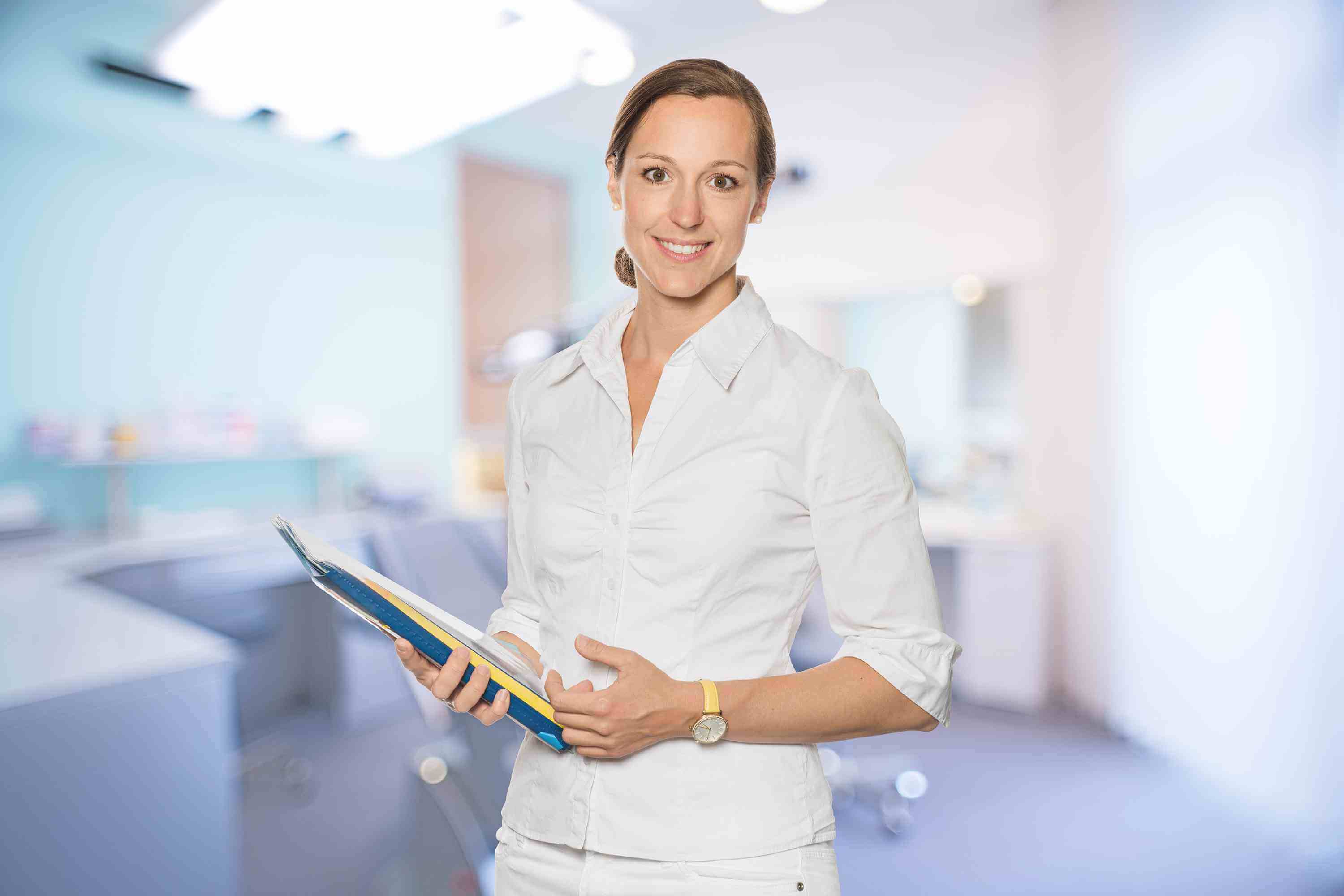 Im Vordergrund die Zahnärztin MSc Kieferorthopädie Dr. Jutta Engeln mit Akten in der Hand, im Hintergrund Behandlungszimmer der Praxis
